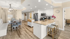 A spacious kitchen with white cabinetry, a large island with stools, and a dining area with a wooden table and chairs. - Gulf-front escape w/ tickets, pool & hot tub (Panama City Beach)