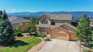 A two-story house with a garage, a front yard with a lawn and trees, and a mountain view in the background. - Air Force Academy Base with Deck and Mountain View (Colorado Springs)