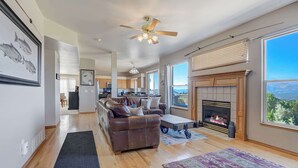 A spacious living room with a fireplace, a leather sofa, and a large window offering a view of the outdoors. - Air Force Academy Base with Deck and Mountain View (Colorado Springs)
