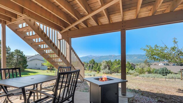 A covered patio with a table and chairs, a fire pit, and a view of mountains and houses. - Air Force Academy Base with Deck and Mountain View (Colorado Springs)