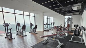 Une salle de sport équipée de divers appareils d’exercice, dotée de grandes fenêtres et offrant une vue sur le paysage urbain.