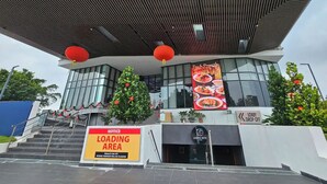 L’extérieur du KOZI SQUARE se distingue par son architecture moderne, avec une entrée imposante, un panneau indiquant la zone de chargement et un bar bien visible appelé LADIES NITE BAR.