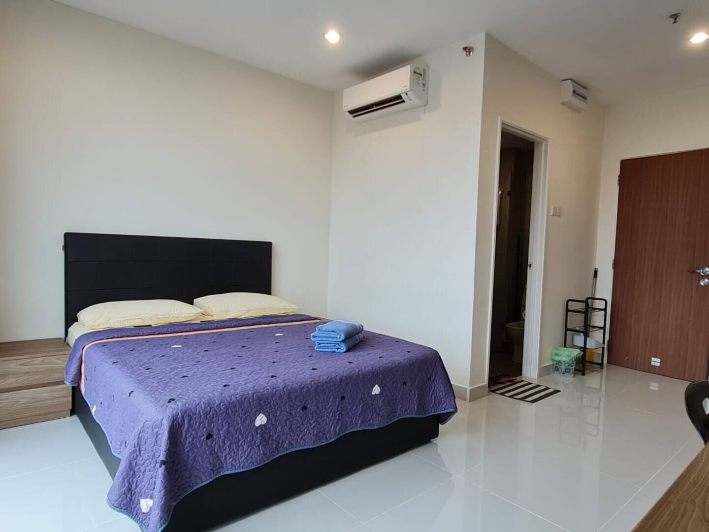 A bedroom with a bed, a wooden floor, and a door leading to another room.