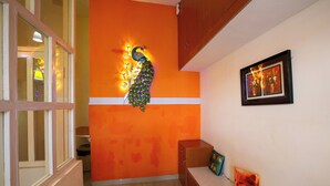 Una stanza con una parete arancione a contrasto, una decorazione a forma di pavone, un quadro incorniciato e una panca con cuscini.
