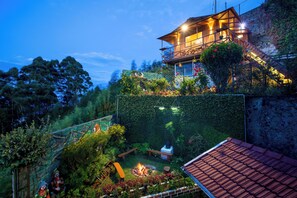 A cozy outdoor patio with a fire pit, wooden furniture, and a stone wall. - Syamantac Villa Kodaikanal (Kodaikanal)