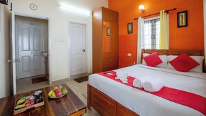 Una camera d'hotel con un letto, un armadio in legno, un comodino con frutta e un vassoio, e una porta che dà su un'altra stanza.