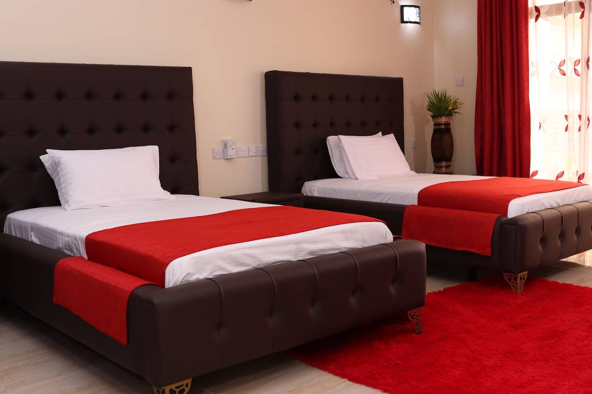 Two beds with dark headboards and red bedspreads in a room with a red carpet.
