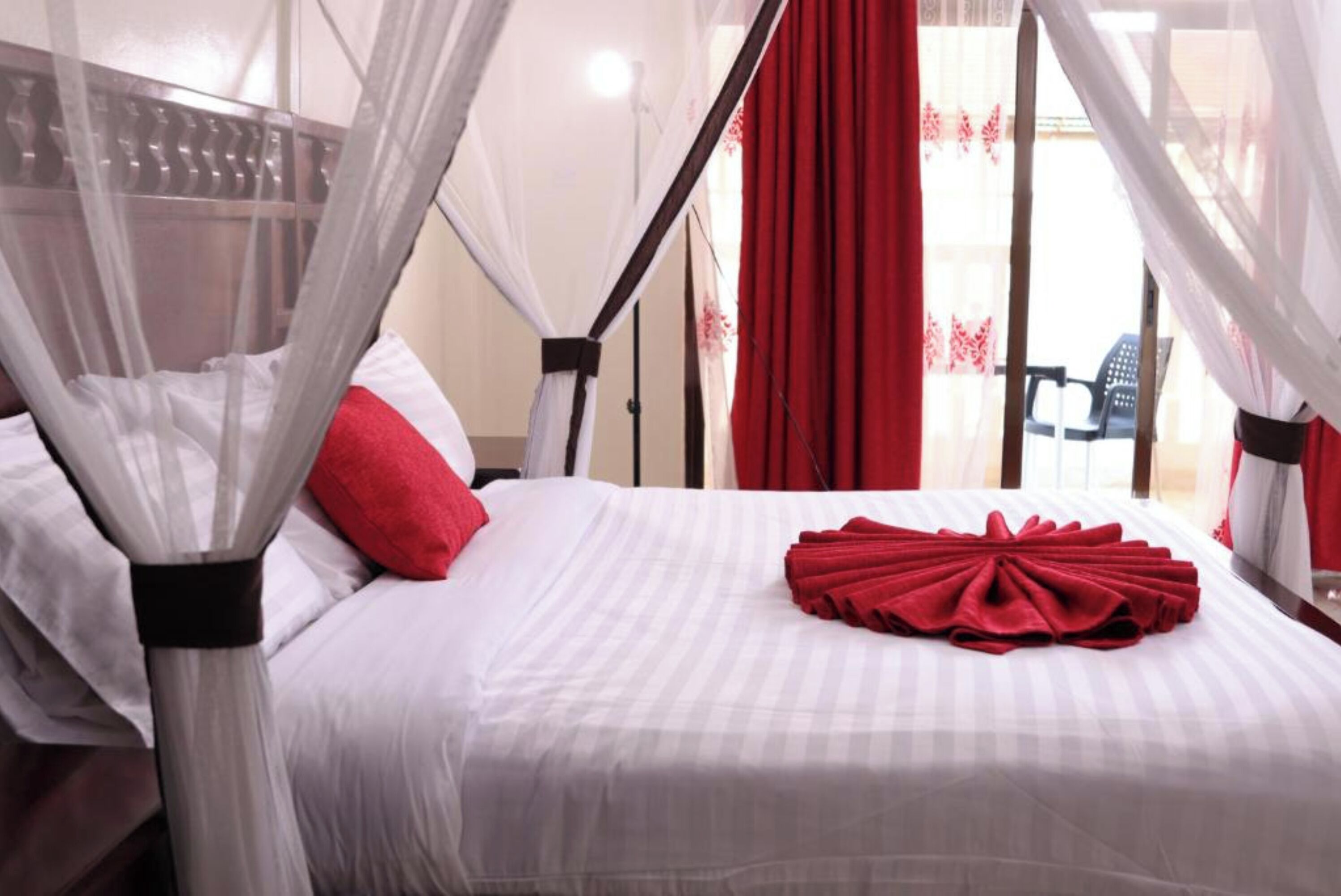Ein Hotelzimmer mit Bett, roten Kissen, einem Baldachin und Blick ins Freie.