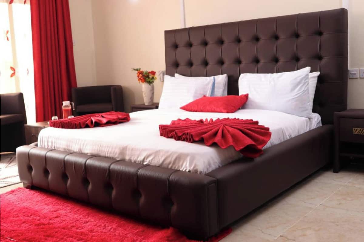 A large bed with a tufted headboard, white bedding, and red accents.