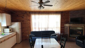 Une chambre confortable, aménagée dans le style d’un chalet, avec un intérieur en bois, une table à manger avec des chaises, un canapé, un coin cuisine équipé d’un four à micro-ondes et d’un réfrigérateur, et une cheminée.