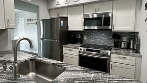 A modern kitchen with stainless steel appliances, a granite countertop, and white cabinetry. - 7 Minute Walk to Beach- Completely Renovated and Pool Views! Two Heated Pool! (Madeira Beach)