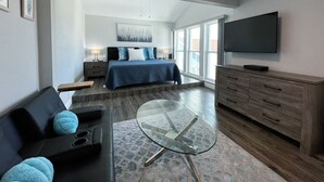A modern hotel room with a large bed, a TV, a glass coffee table, and a sofa. - 7 Minute Walk to Beach- Completely Renovated and Pool Views! Two Heated Pool! (Madeira Beach)