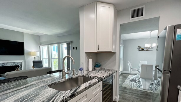 A modern kitchen with a granite countertop, stainless steel appliances, and a dining area with a glass table and chairs. - 7 Minute Walk to Beach- Completely Renovated and Pool Views! Two Heated Pool! (Madeira Beach)
