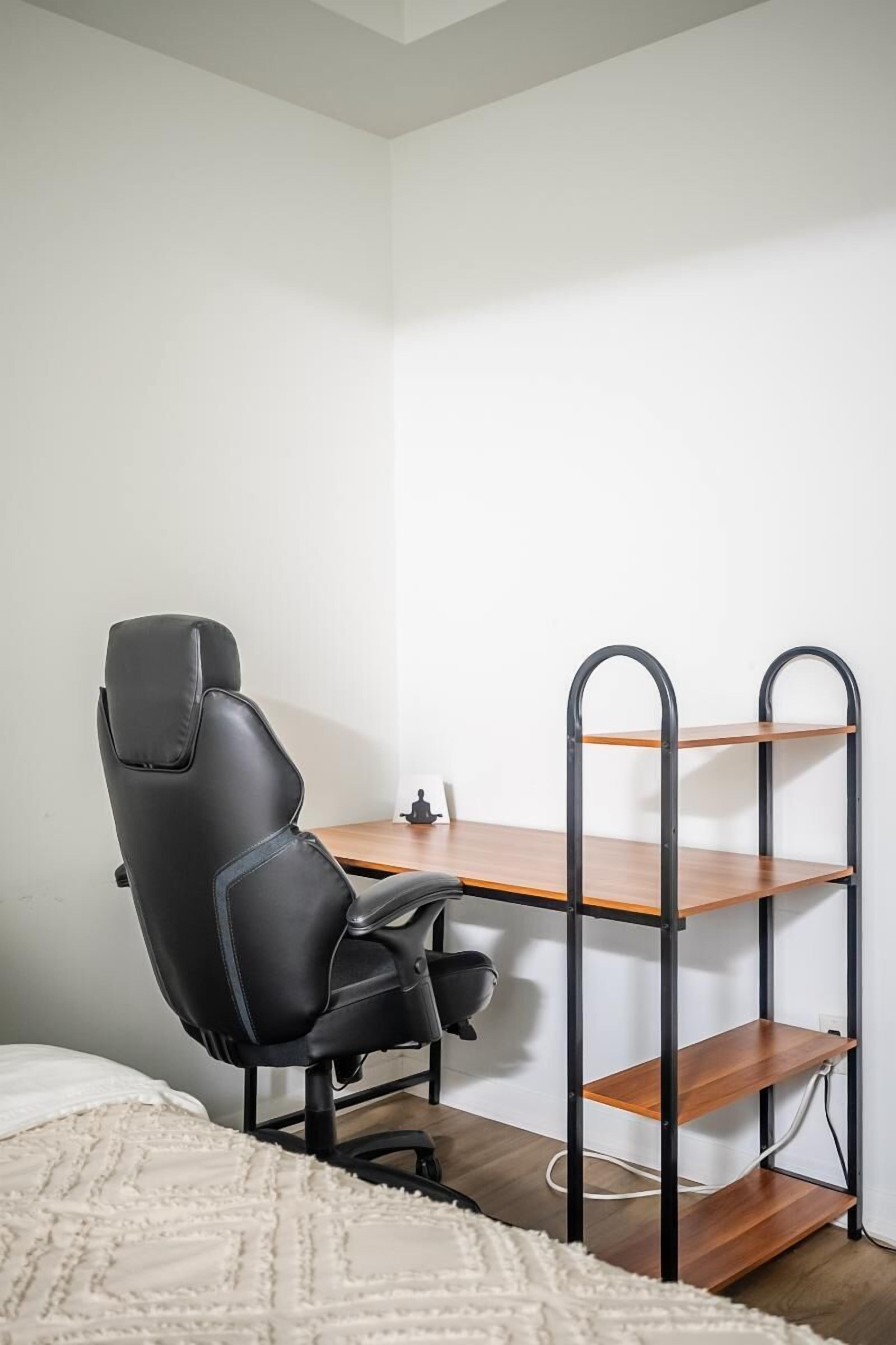 A small, modern room with a black office chair, a wooden desk, and a metal shelving unit.