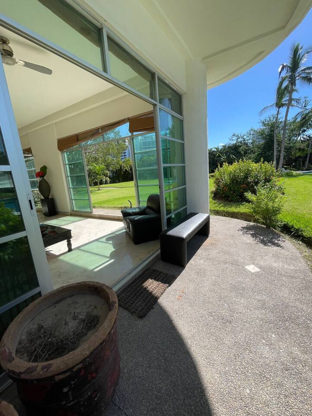 A modern outdoor seating area with a bench and a table, large glass doors leading to a garden, and a potted plant.