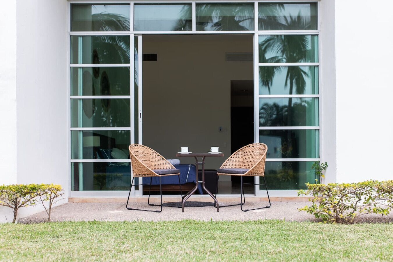 A modern building with large glass doors, two wicker chairs, a small table, and a blue sofa.