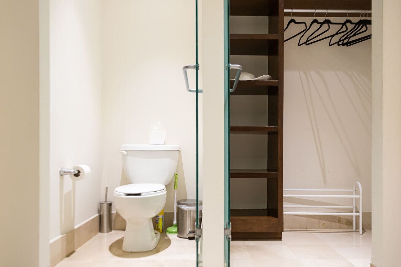 A bathroom with a toilet, a glass shower enclosure, and a wooden shelving unit with hangers.