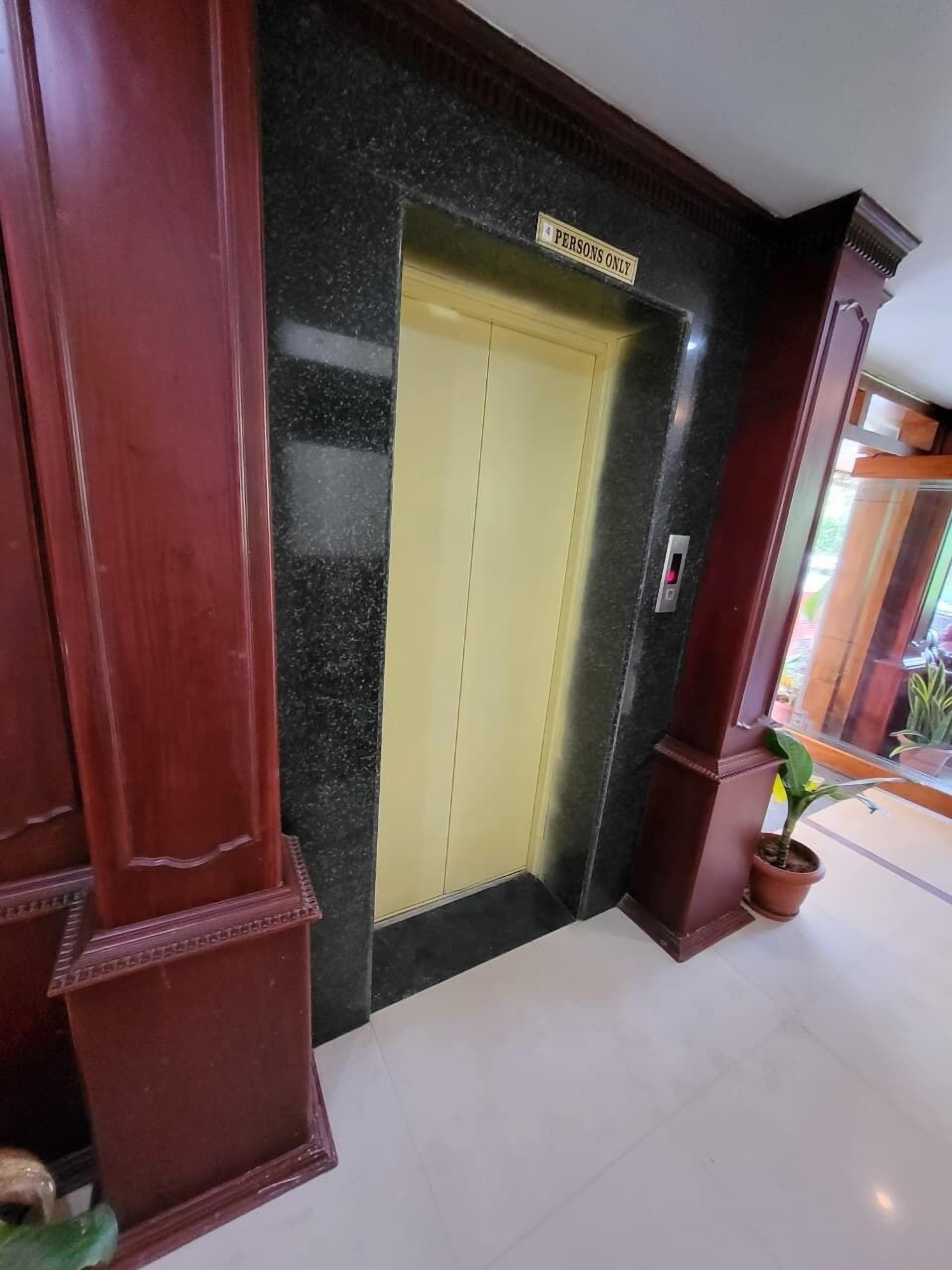 Un pasillo con piso de mármol, un ascensor amarillo y un cartel que indica "solo 4 personas".