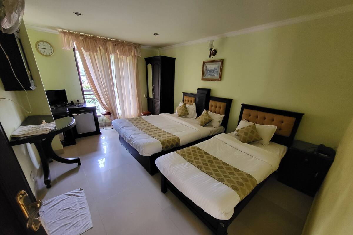 A hotel room with two beds, a desk, a chair, a wardrobe, and a window with curtains.