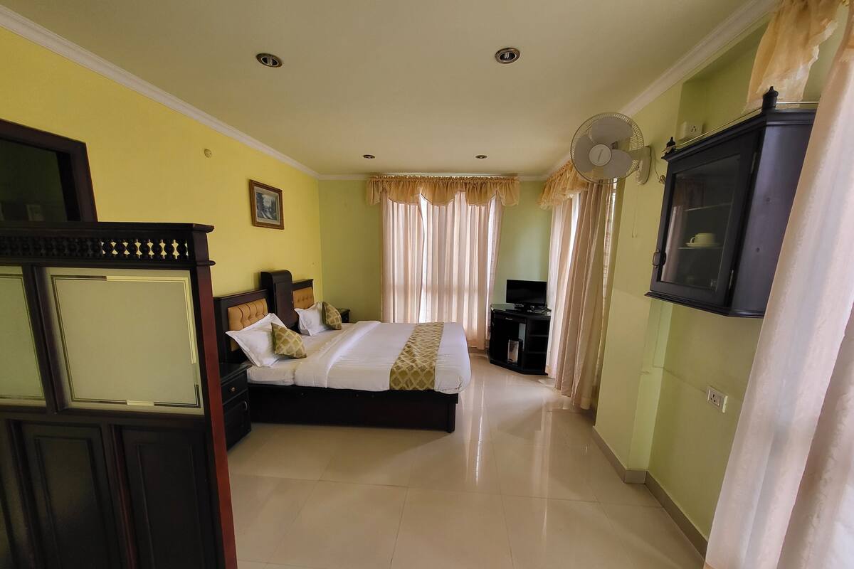 A hotel room with a bed, a TV, a fan, and a cabinet.