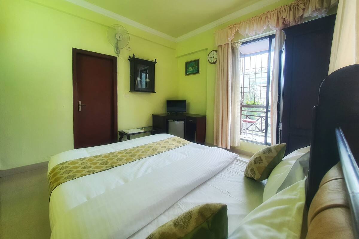 A hotel room with a bed, a desk, a television, a clock, and a window with curtains.
