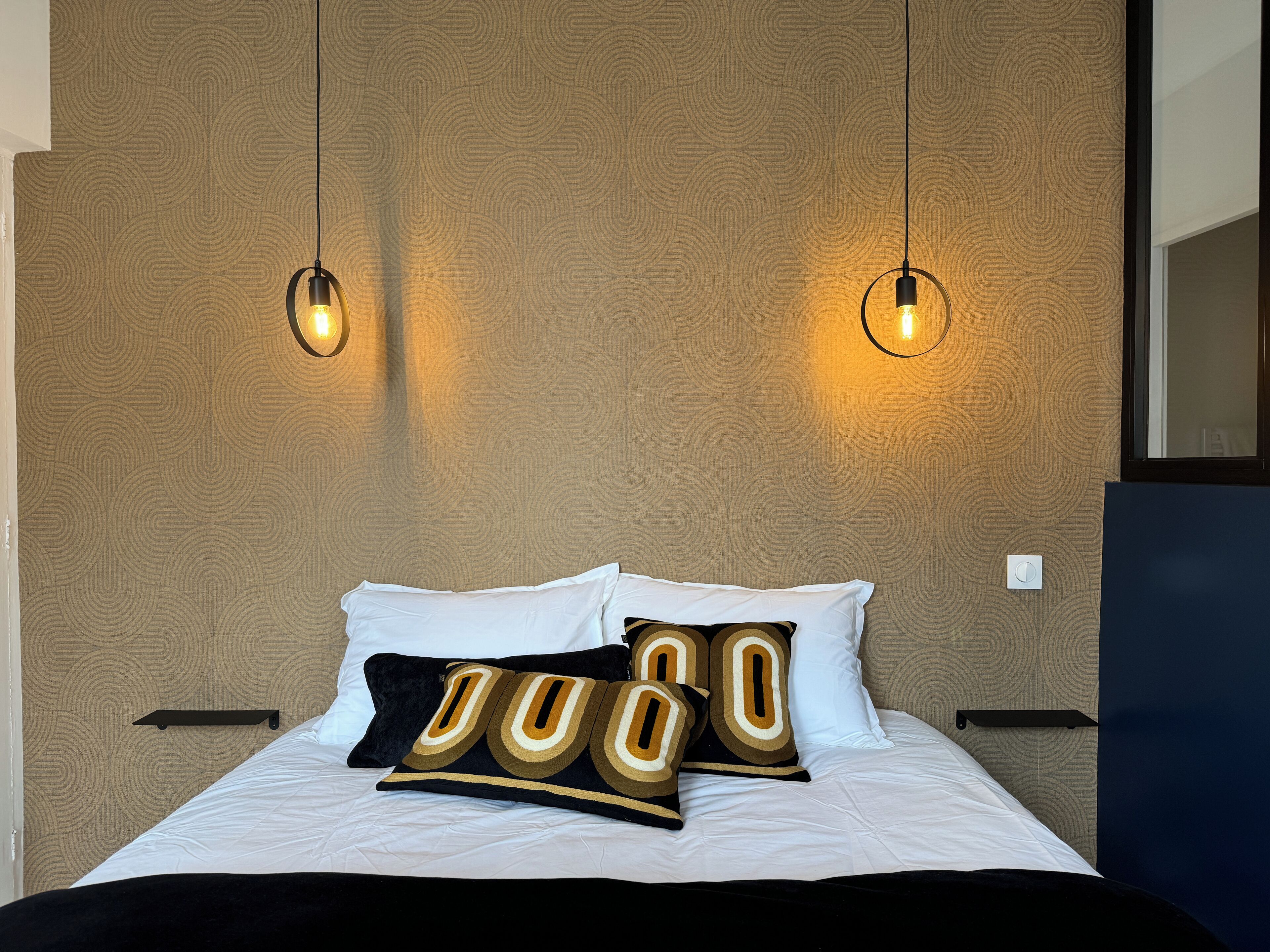 A neatly made bed with white linens and decorative pillows, two wall-mounted light fixtures, and a textured wall pattern.