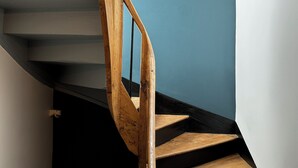 Una escalera espiral de madera con peldaños negros sobre un muro azul.