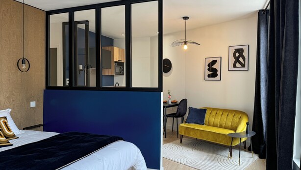 Una habitación de hotel moderna con una cama grande, un sofá, un comedor y una cocina visible a través de un separador de vidrio.