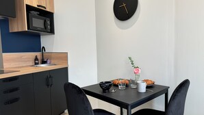 Una cocina moderna con microondas, pileta y muebles de cocina negros. Hay una mesa de comedor con dos sillas, un reloj y un florero con una flor.