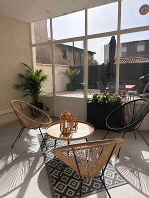Una habitación luminosa con un gran ventanal, sillas de mimbre, una pequeña mesa y un tapete estampado.