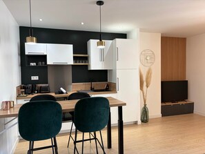 Una cocina moderna con armarios blancos, encimera de madera y dos sillas oscuras.