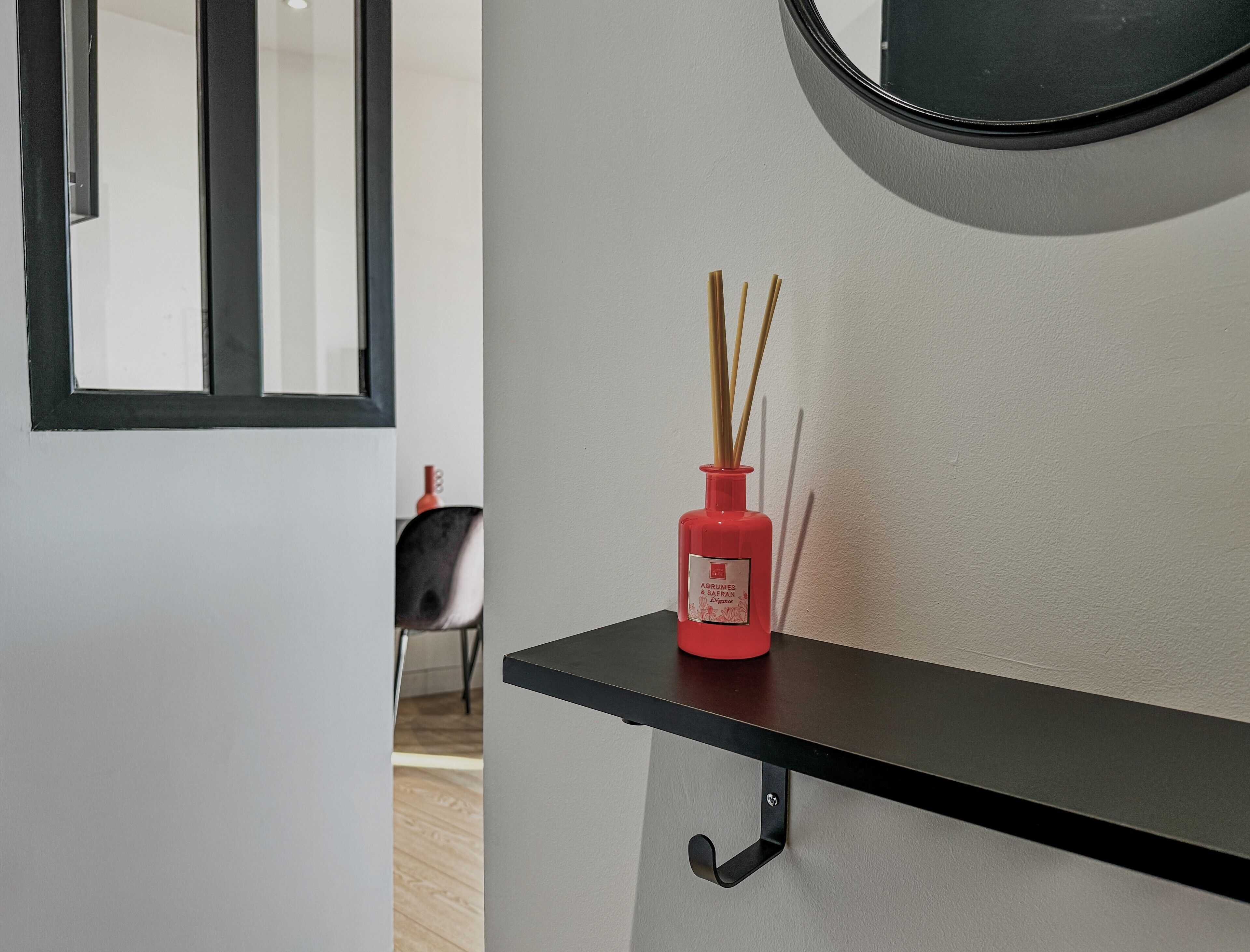 Un intérieur moderne avec une étagère noire sur laquelle est posée une bouteille rouge de diffuseur d’ambiance à bâtonnets, et une chaise noire en arrière-plan.