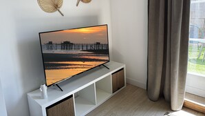 Een televisie op een witte zuil, met uitzicht op een zonsondergang, twee decoratieve wandpanelen en een raam met gordijnen.