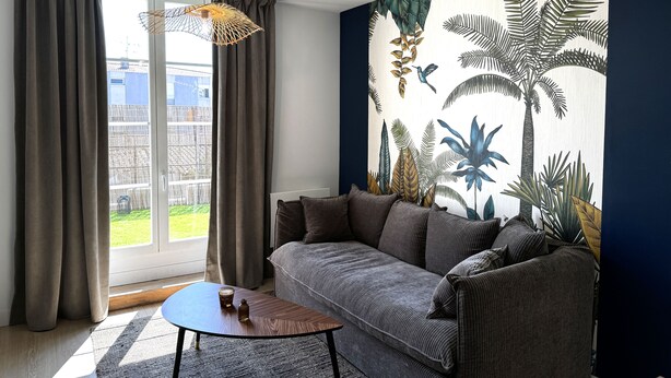 Een woonkamer met een bank, een bijzettafeltje en een groot raam met gordijnen.