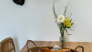 Een houten tafel met een gevlochten mand vol croissants en een vaas met bloemen.