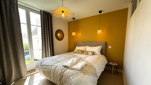 Slaapkamer met een groot bed, een ronde spiegel, twee hanglampen en uitzicht op de omgeving door een schuifdeur.