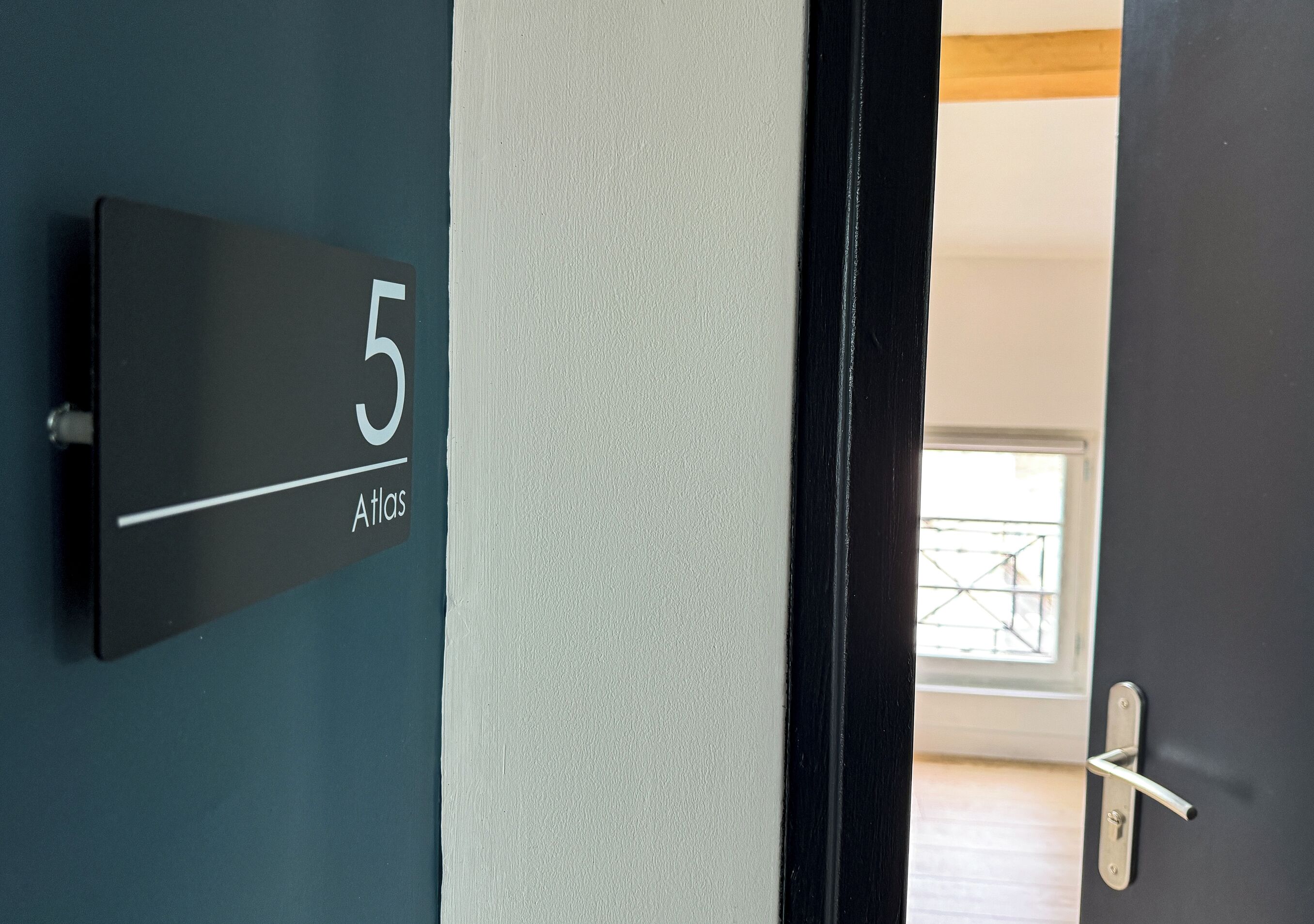 Una puerta con un letrero de número que indica la habitación 5 y la palabra 'Atlas'.