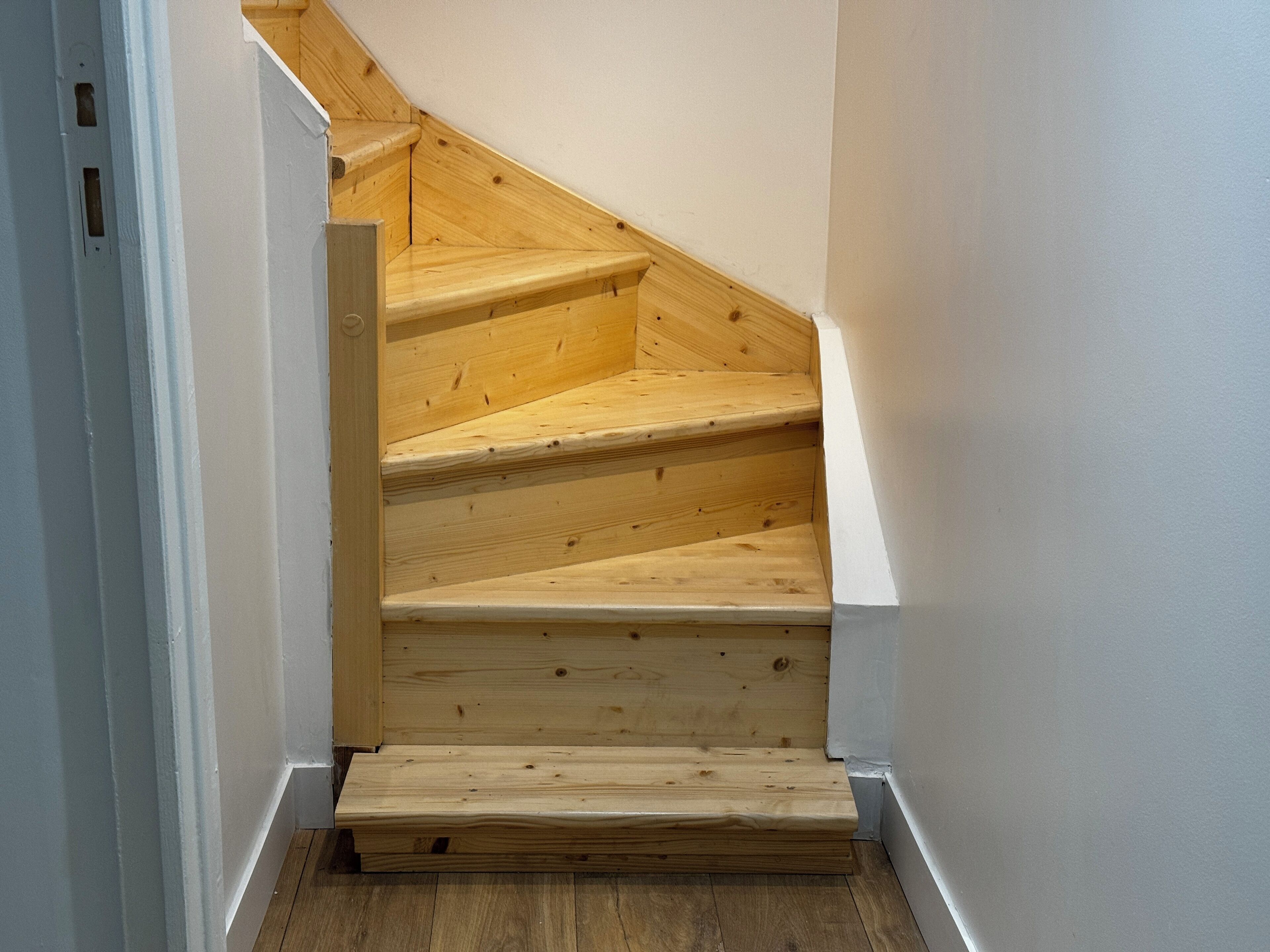 A wooden staircase with a white wall on one side and a wooden floor on the other.