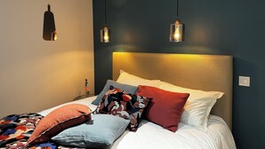 Een slaapkamer met een bed, meerdere kussens, een hoofdeinde en twee hangende hanglampen.