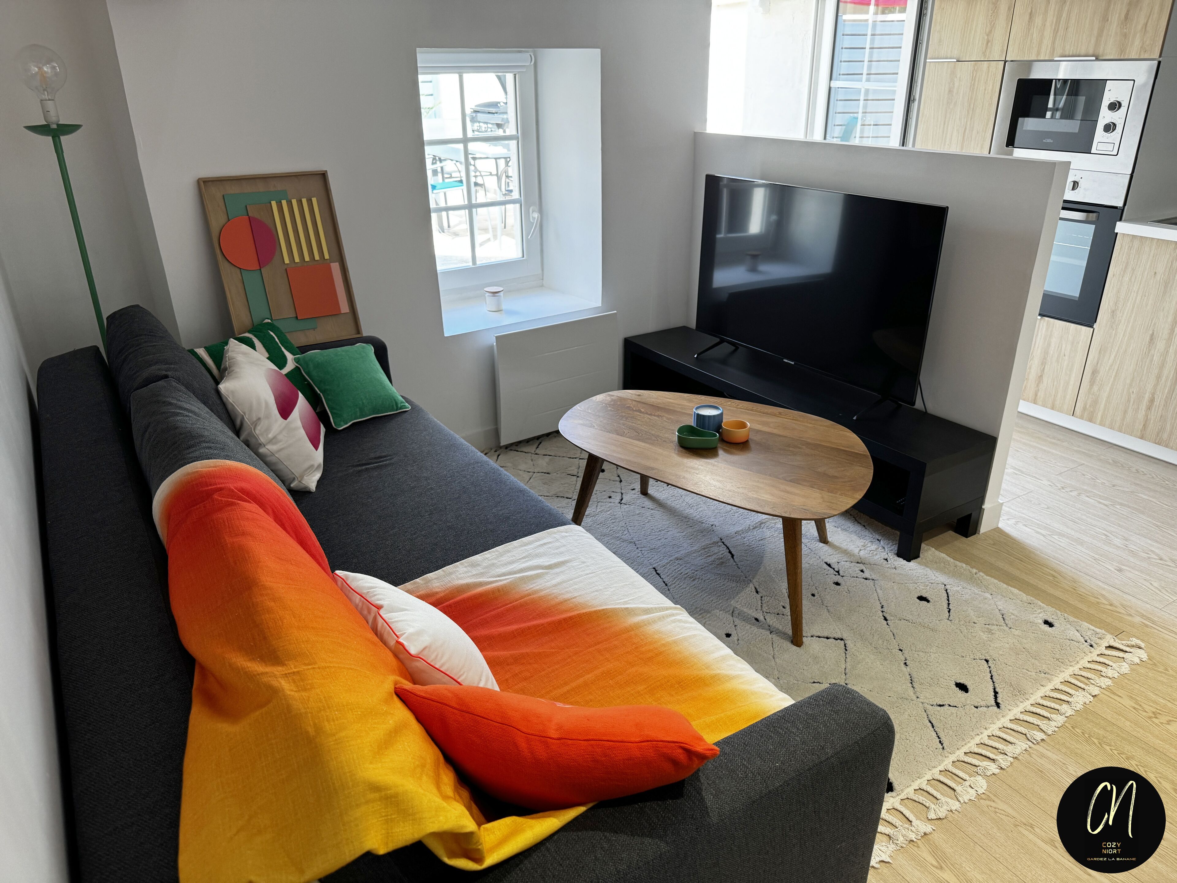 Een moderne woonkamer met een bank, een salontafel, een flatscreen-tv en een keukenhoek met een magnetron.