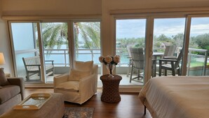 A spacious room with a large bed, a sofa, a chair, and a balcony with a view of the water and palm trees. - 1/1 Waterview Condo, Pool, Private Beach Access (Longboat Key)