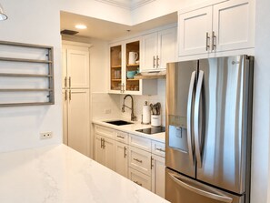 A modern kitchen with white cabinetry, a stainless steel refrigerator, and a marble countertop.