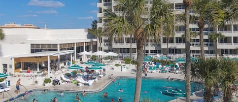 A hotel with a large outdoor swimming pool surrounded by palm trees and lounge chairs.