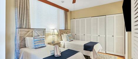 A bedroom with two beds, a ceiling fan, a window with curtains, and a set of white closets.