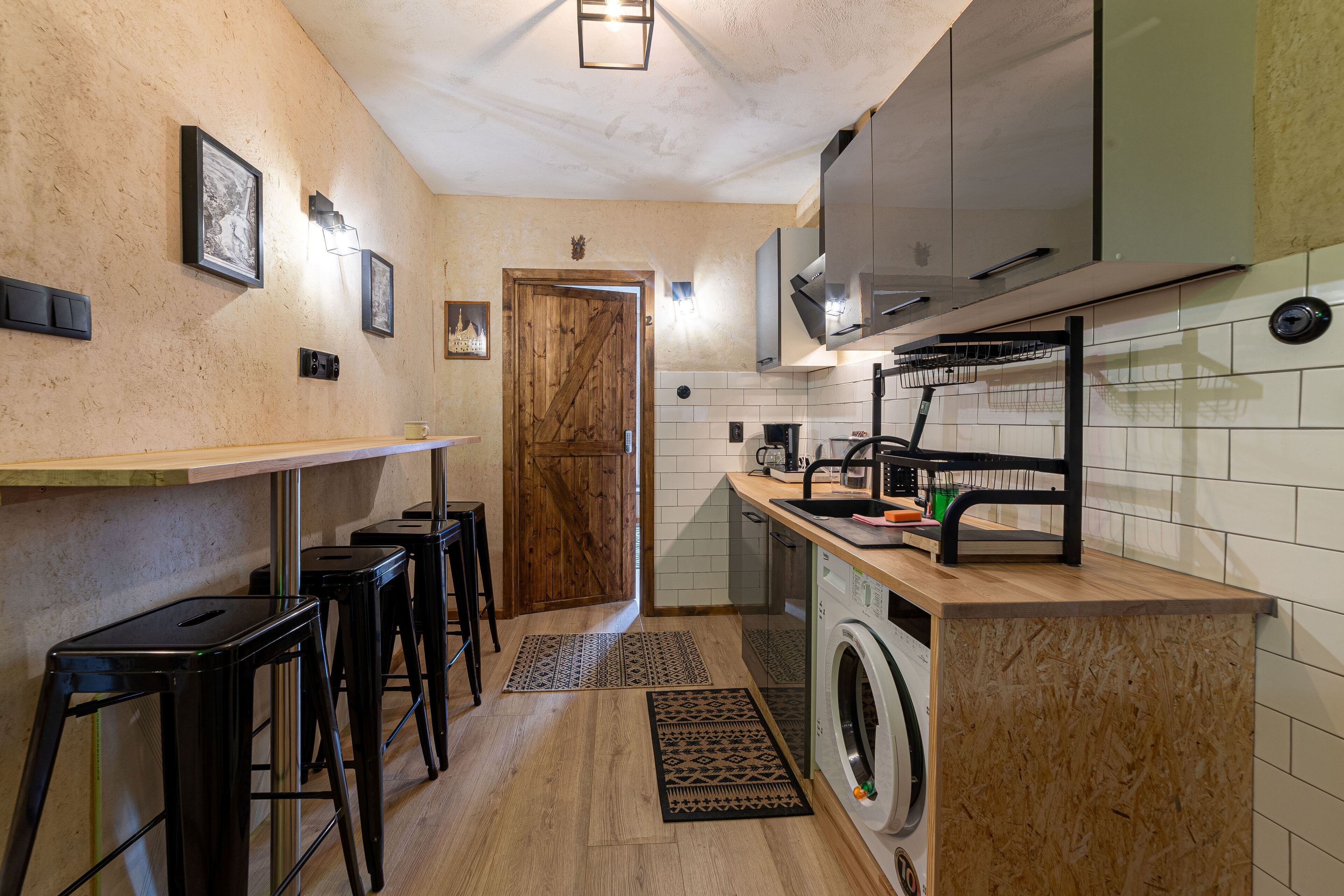 Une cuisine compacte équipée d’un lave-linge, dotée d’une porte en bois et de tabourets de bar.