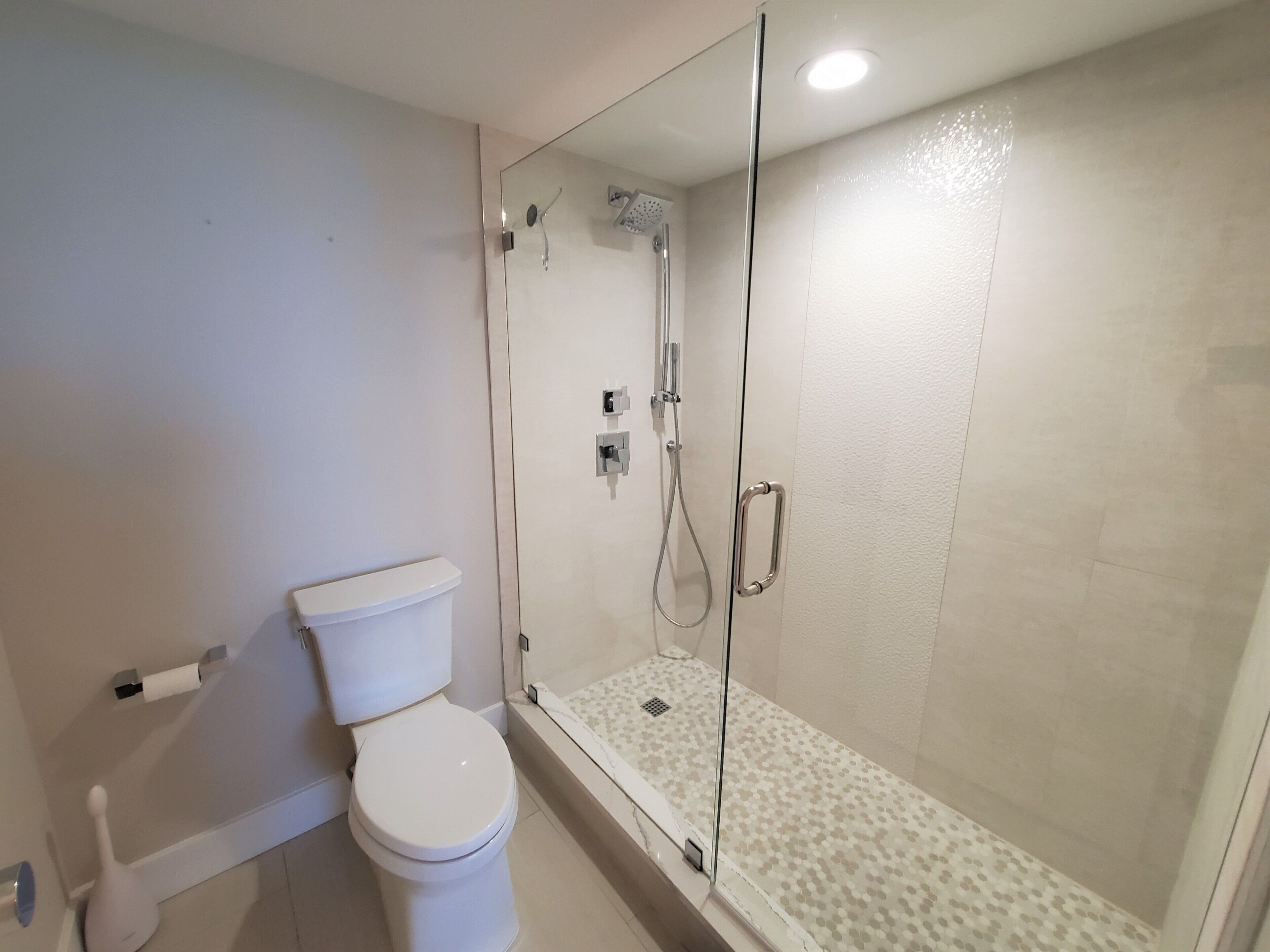 A bathroom with a toilet, a shower with a glass door, and a toilet paper holder.