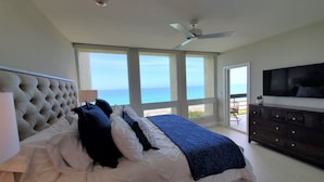 Une chambre avec un grand lit, un ventilateur de plafond et une vue sur l’océan.