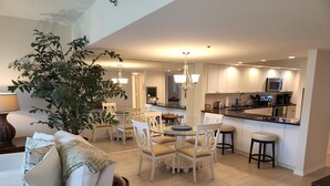 A modern kitchen with white cabinets, a central island, and a dining area with white chairs and a glass table.