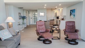 A modern living room with a sofa, two leather recliners, a coffee table, and a dining area with wicker chairs.