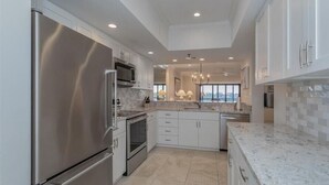 A modern kitchen with stainless steel appliances, white cabinetry, and a marble countertop. - 2/2 Bay Front Condo, Pool, Private Beach Access (Longboat Key)